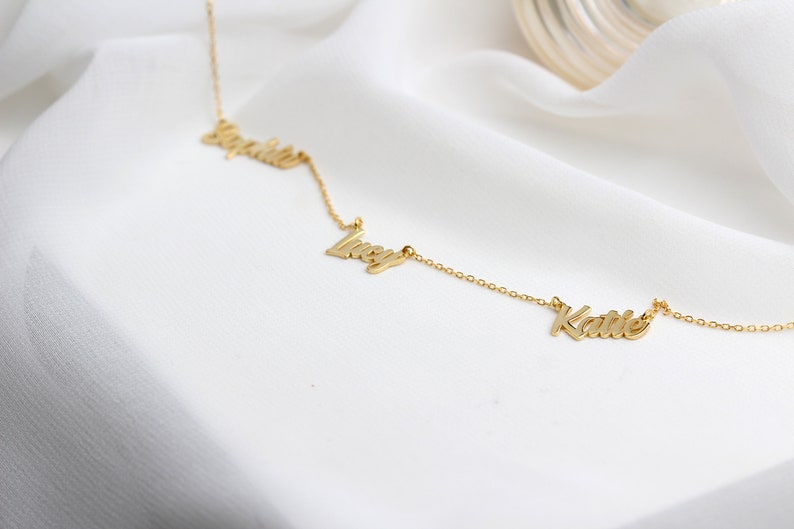 May include: A gold necklace with three names, "Sophia", "Lucy", and "Katie", spelled out in cursive.