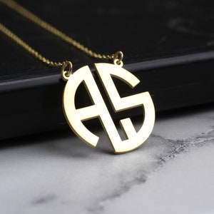 May include: A gold necklace with a circular pendant featuring the letters "AS" intertwined.