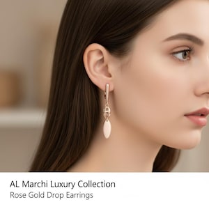 May include: Rose gold drop earrings from the AL Marchi Luxury Collection. The earrings feature a long, slender design with a series of linked circles and a smooth, oval-shaped drop. The earrings are shown on a person.