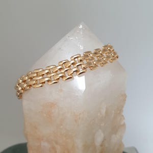 May include: A gold chain bracelet with a square link design. The bracelet is displayed on a white crystal.