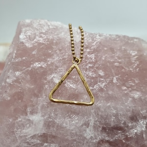 May include: A gold-toned necklace featuring a delicate ball chain and a simple, open triangular pendant with a hammered, textured surface. The pendant hangs from a small circular jump ring attached to the chain, creating a clean geometric design.