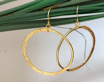 May include: Gold hammered hoop earrings with a textured finish. The earrings are oval shaped and have a simple design.
