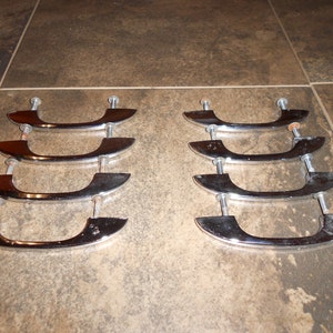 May include: Eight chrome cabinet door pulls with a curved design. The pulls are arranged in two rows of four.