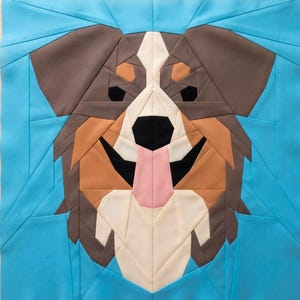 May include: A square fabric quilt block featuring a geometric paper-pieced design of a dog face. The dog has brown ears, tan and white facial markings, a black nose, and a pink tongue, all set against a bright cyan blue background.
