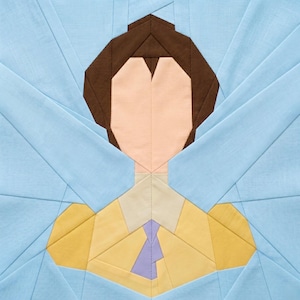 May include: A geometric quilt block featuring a stylized portrait. The face is peach, with brown hair and a yellow shirt with a purple tie. Light blue fabric forms a background with radiating lines, creating a modern, artistic design.