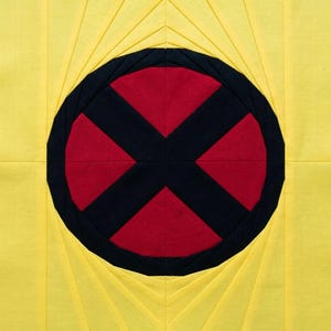 May include: A square, handmade quilt block with a striking design. The centre features a red circle crossed by a black 'X', set within a black border. The background is bright yellow, with radiating pleats.