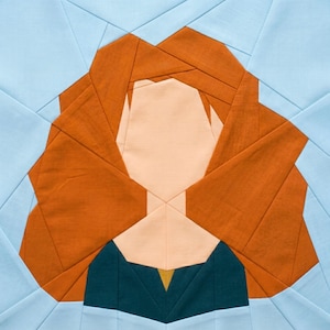 May include: A fabric quilt block featuring a geometric design of a person's face. The hair is a vibrant orange, the face is peach, and the clothing is teal with a gold accent. The background is light blue.