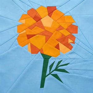May include: A geometric fabric art piece featuring a marigold flower. The flower is composed of orange and yellow fabric pieces, with a green stem and leaves. The background is light blue, with geometric lines.