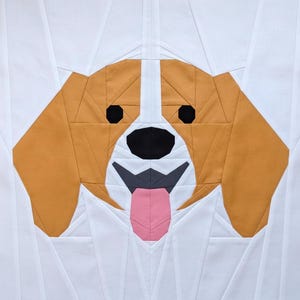 May include: A fabric dog face quilt block. The dog has brown and white fur, black eyes, and a pink tongue. The block is made of geometric shapes and is set against a white background.