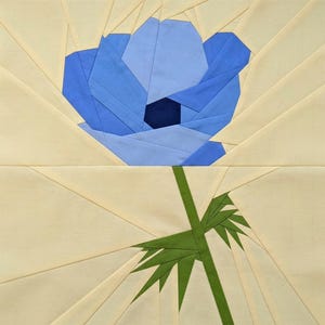 May include: A fabric art piece featuring a blue flower with a dark center, green stem, and leaves. The flower is made of various shades of blue fabric. The background is a light beige color with radiating lines.