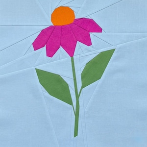 May include: A fabric block featuring a geometric design of a flower. The flower has a bright pink petal, an orange center, and a green stem and leaves. The background is light blue.