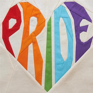 Peut inclure: Un bloc de courtepointe en tissu représentant le mot PRIDE assemblé en forme de cœur. Les lettres sont construites à partir de segments de tissu unis rouge, orange, vert, bleu clair et violet sur un fond de tissu de couleur crème.