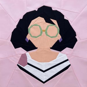 May include: A geometric quilt block featuring a stylized portrait of a person. The face is peach-colored with green glasses and black hair. The person is wearing a white top with black stripes and a pink jacket.