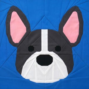 May include: A geometric quilt block featuring a French Bulldog's face. The dog's face is primarily black, white, and gray, with pink ears and a white stripe down the center of its face. The background is a vibrant blue.
