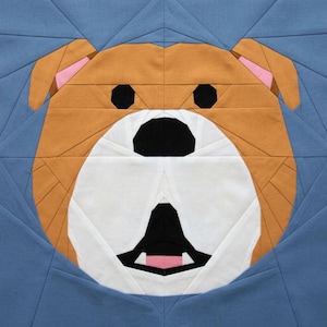 May include: A fabric art piece featuring a bulldog's face. The dog's face is constructed from geometric shapes in shades of tan, white, black, and pink, set against a blue background. The bulldog's eyes and nose are black, and the ears have pink accents.