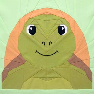 May include: A green and orange turtle face quilt block. The turtle has large black and white eyes, a smiling mouth, and a geometric design. The background is a light green color.