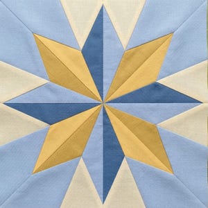 Pode incluir: Um bloco de colcha geométrico com um design de estrela. A estrela é composta por peças de tecido azul, azul claro, creme e dourado. O centro da estrela é azul escuro, com pontas radiantes em dourado e azul claro.