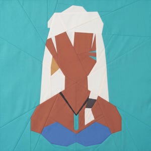 May include: A geometric quilt featuring a stylized portrait of a person with brown skin, white hair, and a blue top. The quilt is made of various fabric pieces in shades of brown, white, blue, and teal, with a teal background.