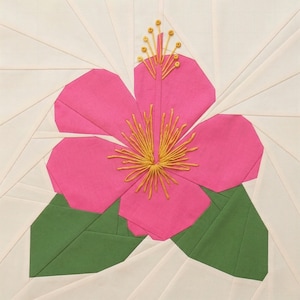 Puede incluir: Un vibrante diseño floral geométrico de tela. La flor presenta pétalos de color rosa brillante, un centro amarillo y hojas verdes. El fondo es de color crema claro con un patrón geométrico. La flor es probablemente parte de un proyecto de edredón o arte textil.