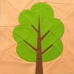 May include: A fabric art piece featuring a stylized tree. The tree has a brown trunk and branches, with a bright green, rounded crown. The background is a light peach color with geometric lines, creating a patchwork effect. The artwork is likely a quilt block.
