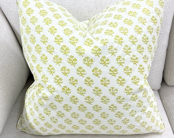 May include: A white throw pillow with a yellow floral pattern. The pillow is sitting on a white couch.