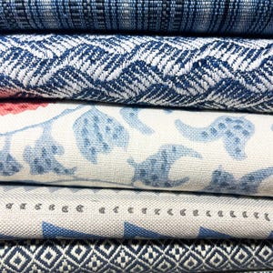 May include: A stack of six folded fabric swatches featuring various patterns. The top layer is dark blue with thin stripes, followed by a blue and white chevron weave, a white fabric with blue floral prints, a light gray with small dots, a blue diamond pattern, and a bottom layer with thin multicolored stripes.