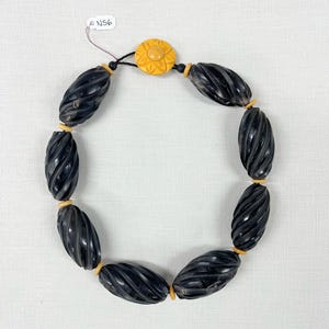 May include: A black and yellow necklace with a carved flower pendant and twisted black beads.