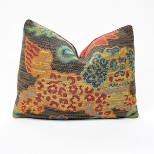 May include: Decorative throw pillow with a detailed, colorful design. The pillow features a brown background with a pattern of a mythical creature in shades of orange, yellow, blue, and red. The pillow is rectangular and appears to be made of woven fabric.