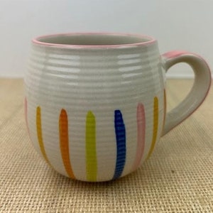 May include: White ceramic mug with a pink rim and colorful vertical stripes in yellow, orange, blue, and pink.