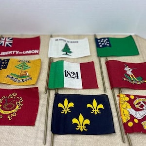 May include: A collection of small flags with various designs and colors. The flags include the text "LIBERTY-UNION", a green tree, a green flag with blue stars, and a flag with the number "1824".