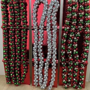 May include: Three decorative Christmas displays. Two feature red, green, and silver bell garlands, while the center one showcases silver bell garlands. All are mounted on red rectangular backgrounds.