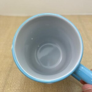 Op de afbeelding: Een lichtblauwe keramische mok met een witte binnenkant. De mok heeft een afgeronde handgreep.