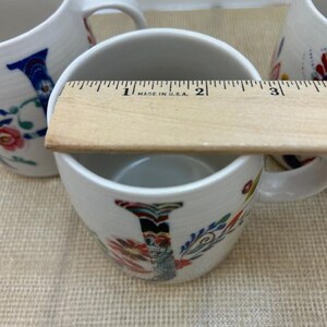 Puede incluir: Tazas de cer&aacute;mica blanca con dise&ntilde;os florales y la letra "I". Las tazas tienen aproximadamente 7,6 cm de di&aacute;metro. Las tazas tienen un asa y est&aacute;n decoradas con coloridos estampados florales y la letra "I".