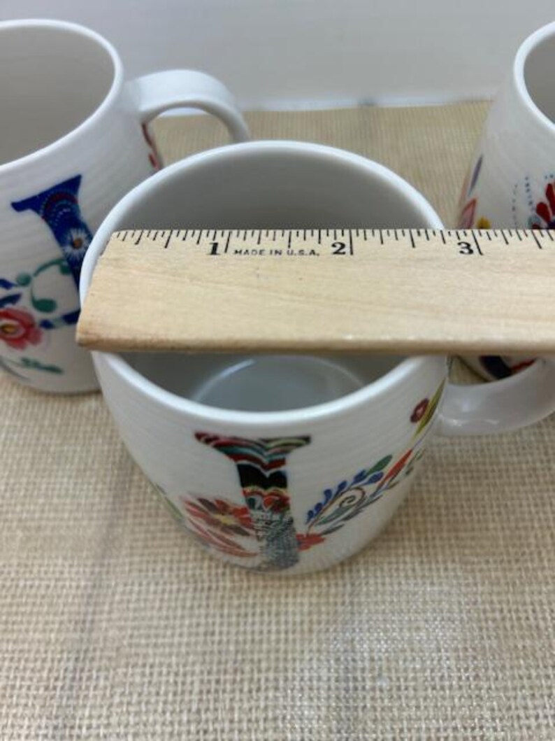 Puede incluir: Tazas de cer&aacute;mica blanca con dise&ntilde;os florales y la letra "I". Las tazas tienen aproximadamente 7,6 cm de di&aacute;metro. Las tazas tienen un asa y est&aacute;n decoradas con coloridos estampados florales y la letra "I".