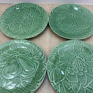 May include: Four green ceramic plates with embossed fruit and leaf designs. Two plates feature pears, and two feature clusters of berries. The plates are round and have a glossy finish, perfect for serving fruit or desserts.