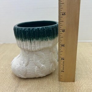 Pu&ograve; includere: Un piccolo vaso in ceramica a forma di calzino. La parte superiore &egrave; verde scuro, che sfuma nel bianco con un motivo a trecce. Un righello di legno misura circa 13 cm.
