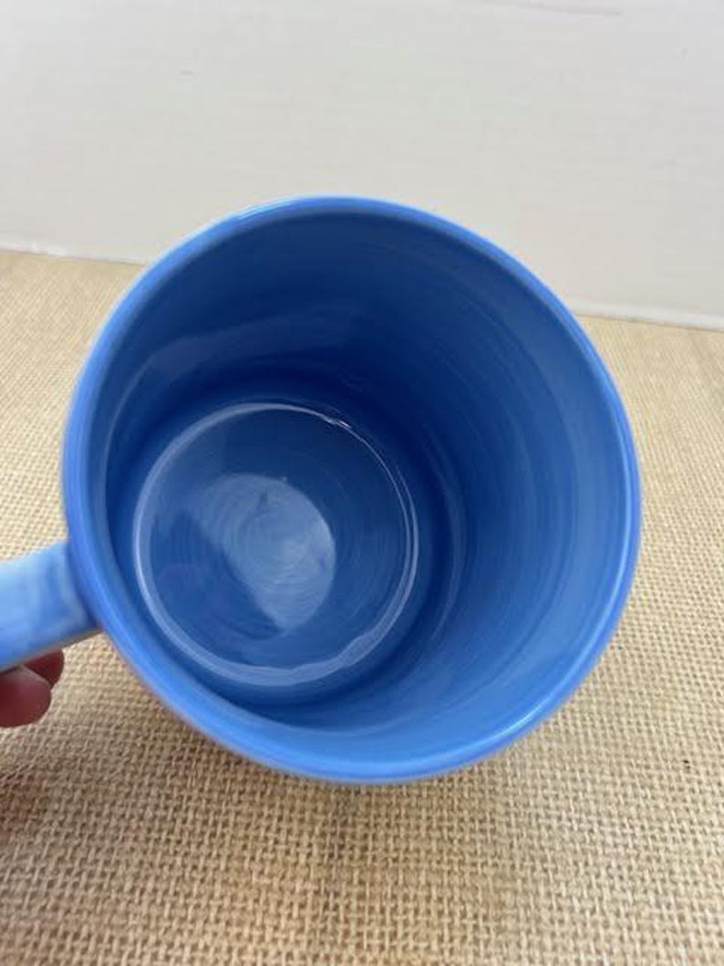 May include: A light blue ceramic mug with a handle. The interior and exterior of the mug are a solid light blue color. The mug is empty and appears to be clean.