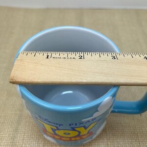 Op de afbeelding: Een blauwe keramische mok met een wit wolkenontwerp en de woorden "Disney Pixar Toy Story" erop gedrukt. De mok heeft een diameter van 7,6 cm.