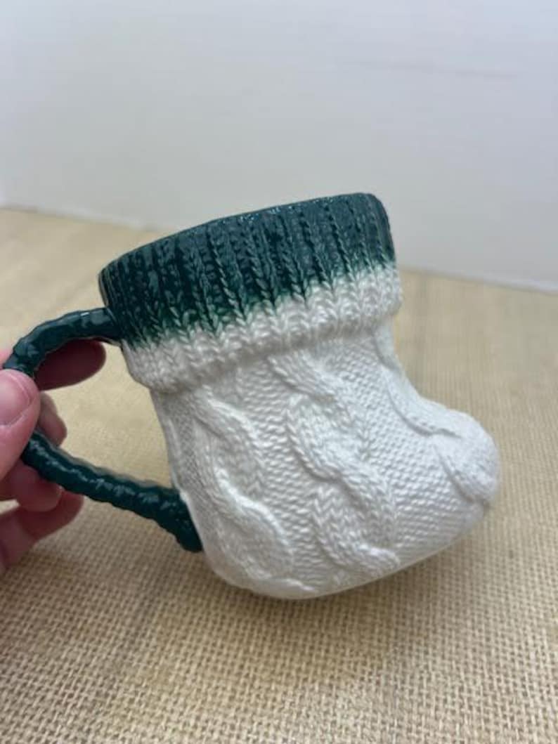 Pu&ograve; includere: Una tazza in ceramica a forma di calzino, con un motivo a trecce bianco e un bordo e manico verde scuro. La tazza &egrave; progettata per assomigliare a un caldo calzino invernale.