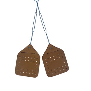 May include: Two brown leather fly swatters with metal handles. The handles are crossed and the swatters are hanging.