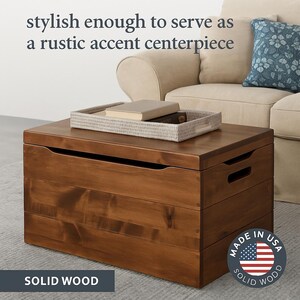 May include: A solid wood storage chest with a rich brown finish. The chest has a rectangular shape with a flat top and integrated handles. A woven tray with books sits on top. The text "stylish enough to serve as a rustic accent centerpiece" is visible.