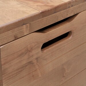 May include: Close-up of a wooden storage box with a natural finish. The box features a recessed handle for easy opening and closing. The wood grain is visible, and the box appears to be well-crafted.