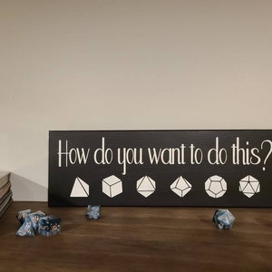 May include: Black wooden sign with white text that reads "How do you want to do this?" with six white dice icons in a row below the text. The dice icons are a four-sided die, a six-sided die, an eight-sided die, a ten-sided die, a twelve-sided die, and a twenty-sided die.