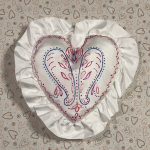 Könnte beinhalten: Weißes herzförmiges Kissen mit einem Rüschenrand und einem blauen und rosa floralen Design.