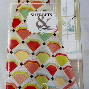 Könnte beinhalten: Ein Quilt-Musterbuch mit dem Titel "Sherbets & Creams" mit einem farbenfrohen Quilt-Design. Der Quilt hat ein sich wiederholendes Muster aus fächerförmigen Blöcken in Rot, Gelb, Grün und Pfirsich, mit schwarzen quadratischen Akzenten auf weißem Hintergrund.