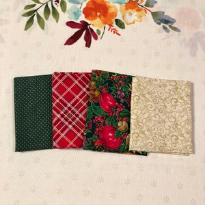 May include: Five folded fabric squares with festive holiday patterns. The fabrics include a dark green with gold polka dots, red plaid, a dark green with red berries and pomegranates, and a cream-coloured fabric with gold swirls.
