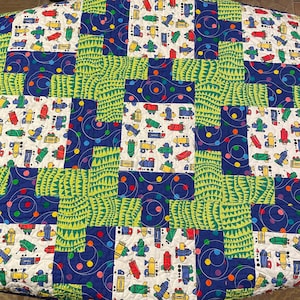 May include: A patchwork quilt with a blue background and green, white, and yellow squares. The squares feature a repeating pattern of toy airplanes and crayons. The quilt is decorated with blue and yellow polka dots.