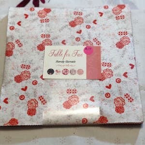 May include: A white fabric with a red floral pattern and small hearts. The fabric is labeled "Table for Two" by Sandy Gervais Moda.