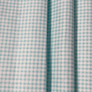 Op de afbeelding: Een close-up van een lichtblauwe en witte gingham stof. De stof is in drieën gevouwen, waardoor het patroon zichtbaar is.