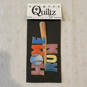 Puede incluir: Una tarjeta negra con las palabras "Quiltz Appliques" impresas en ella. La tarjeta tiene una aplicación colorida de un bate de béisbol, una pelota de béisbol y las palabras "Home Run" en ella.